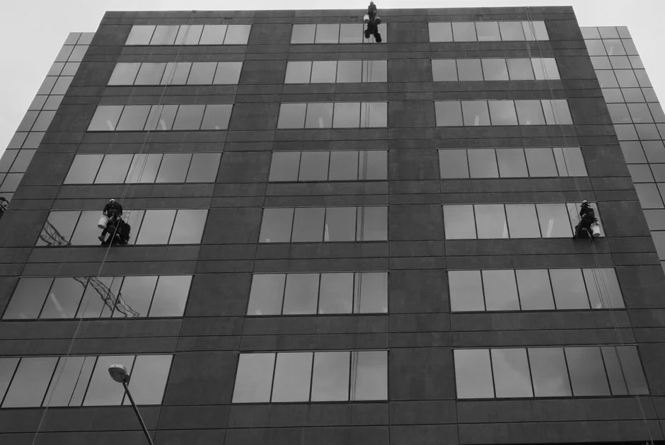 Two workers clean windows on a modern glass building facade using a suspended platform.